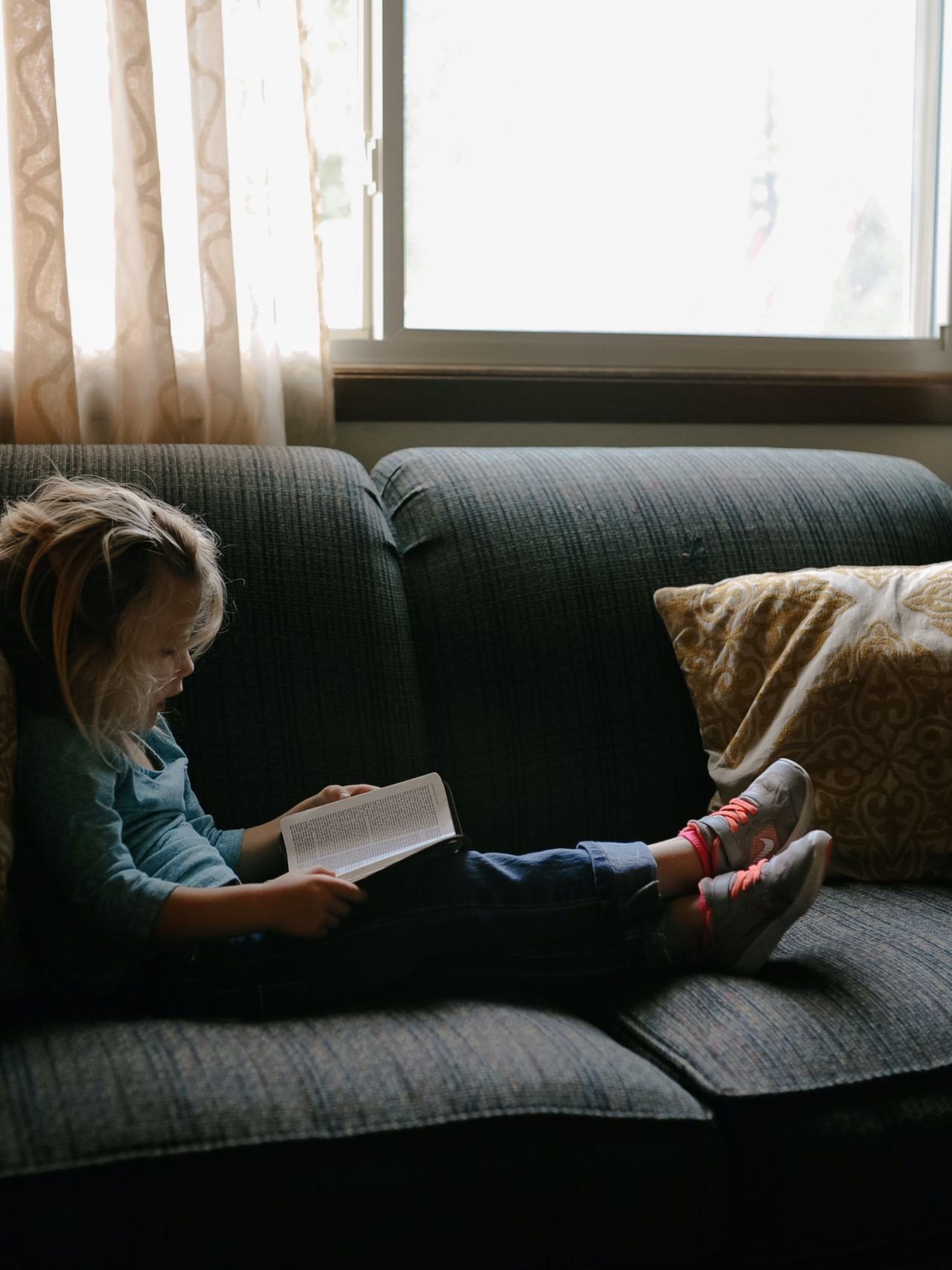 girl reading book sitting on sofa