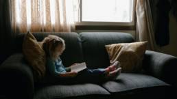 girl reading book sitting on sofa