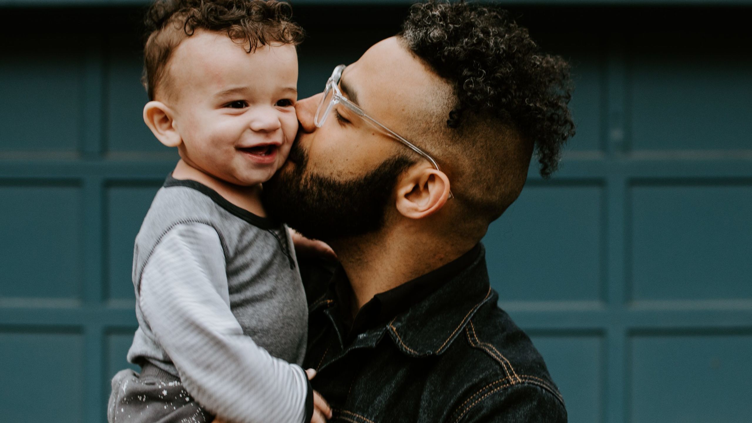 man carrying baby boy and kissing on cheek