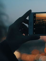 person capturing photo of city using iPhone during orange sunset