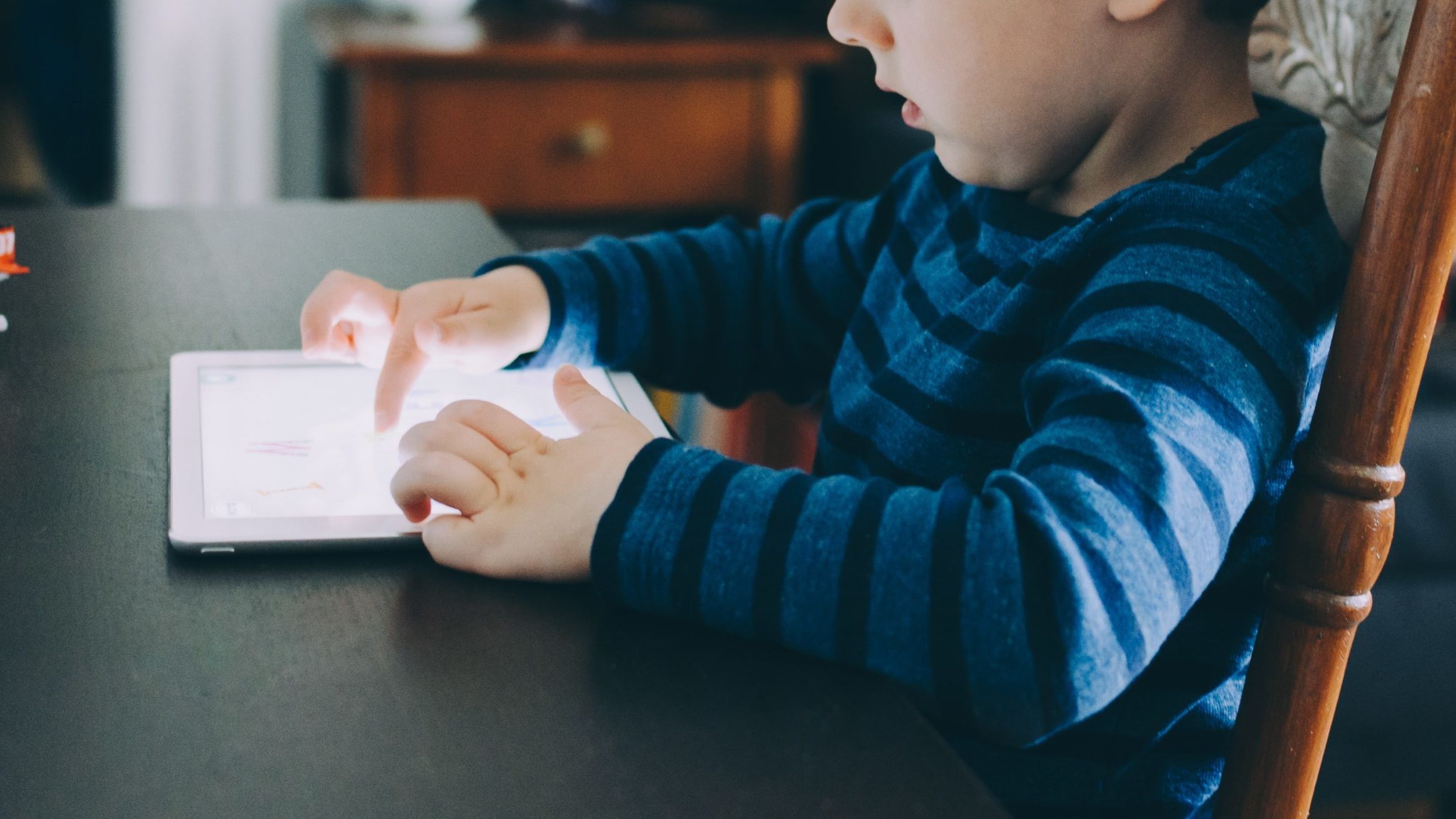 boy sitting on chair beside table using tablet computer