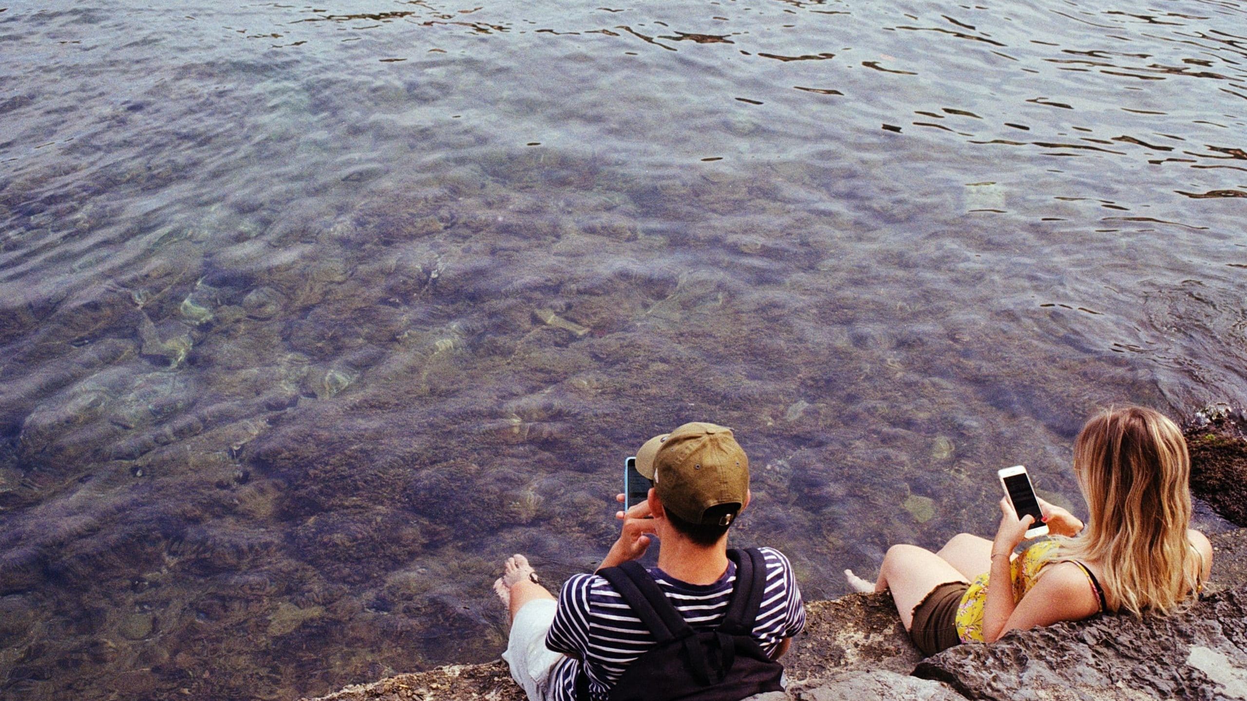 man in black and white stripe shirt sitting on rock near body of water during daytime