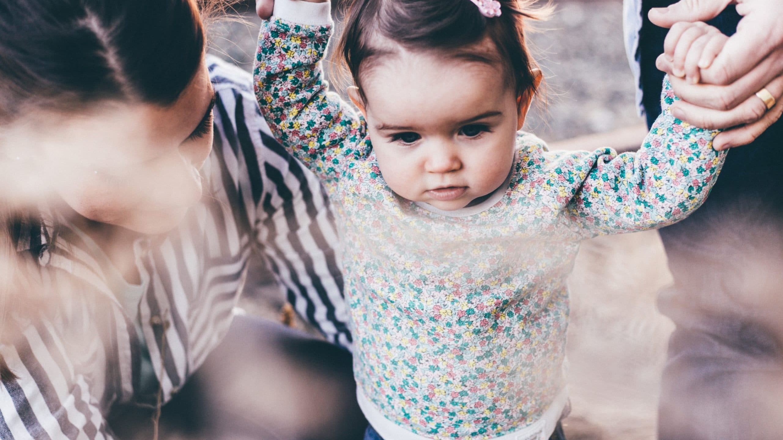 woman holding girl while learning to walk taken at daytime