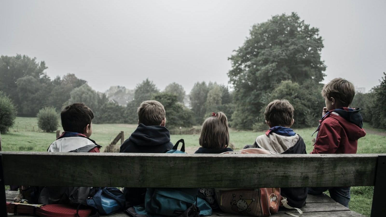 five children sitting on bench front of trees