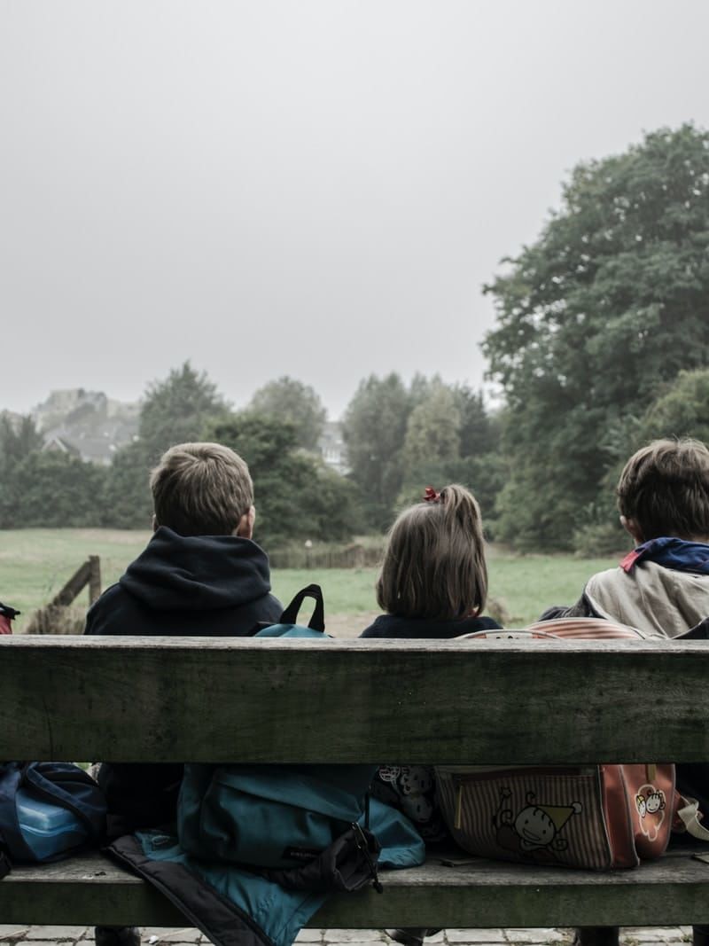 five children sitting on bench front of trees