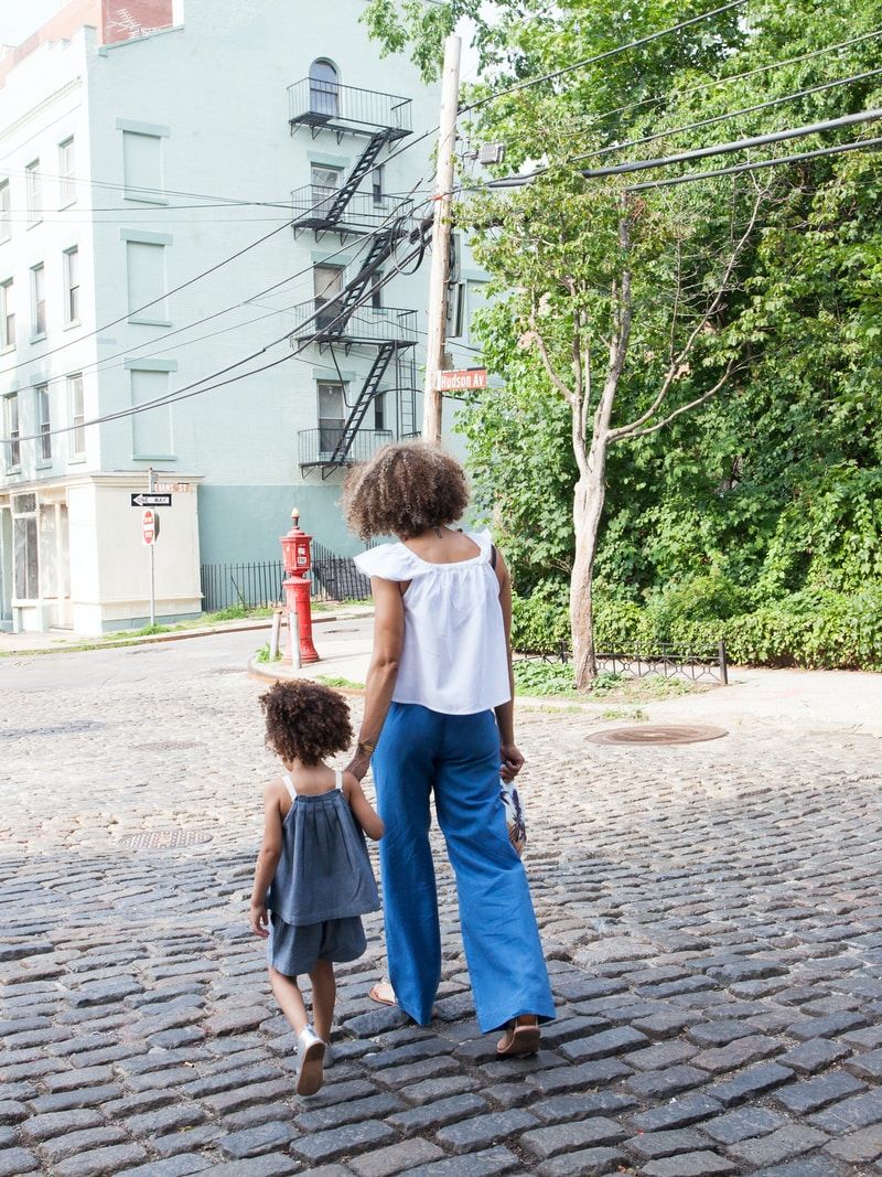 woman in white cap-sleeved shirt and blue pants walking beside girl in gray tank top