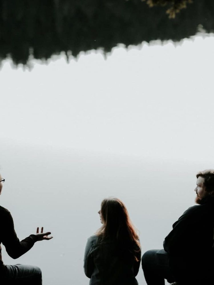 silhouette of three people sitting on cliff under foggy weather