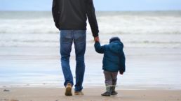 man and boy walking on seashore under blue sky