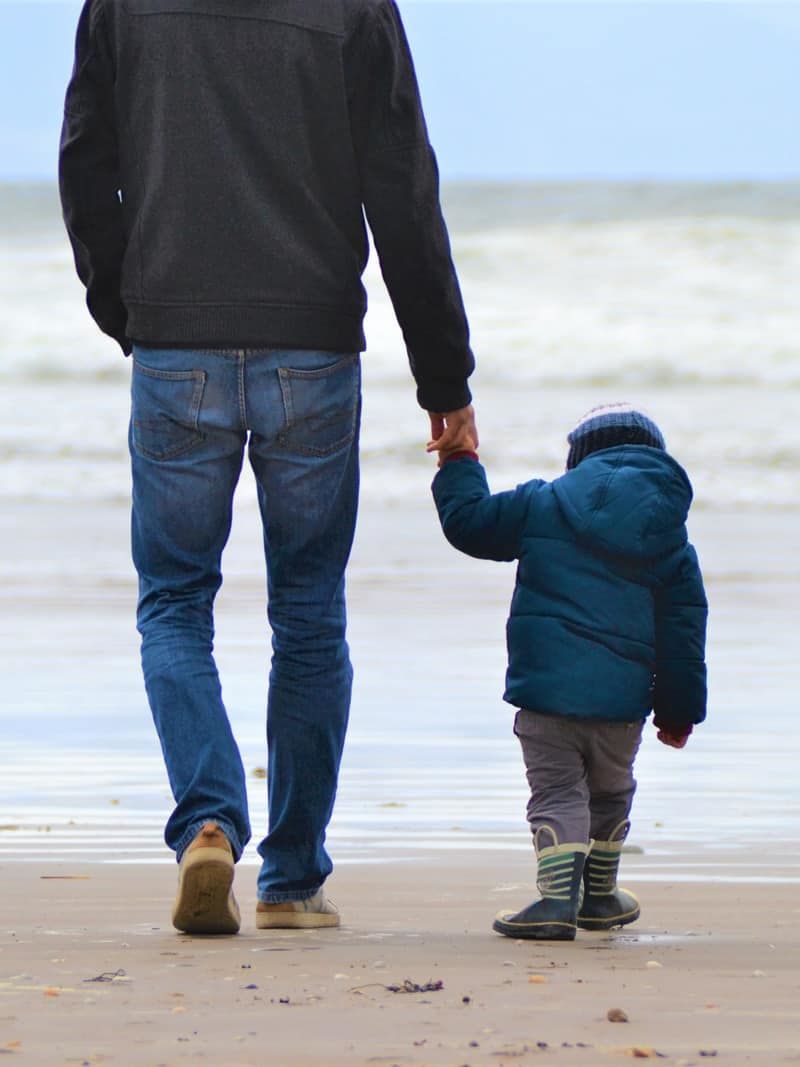 man and boy walking on seashore under blue sky