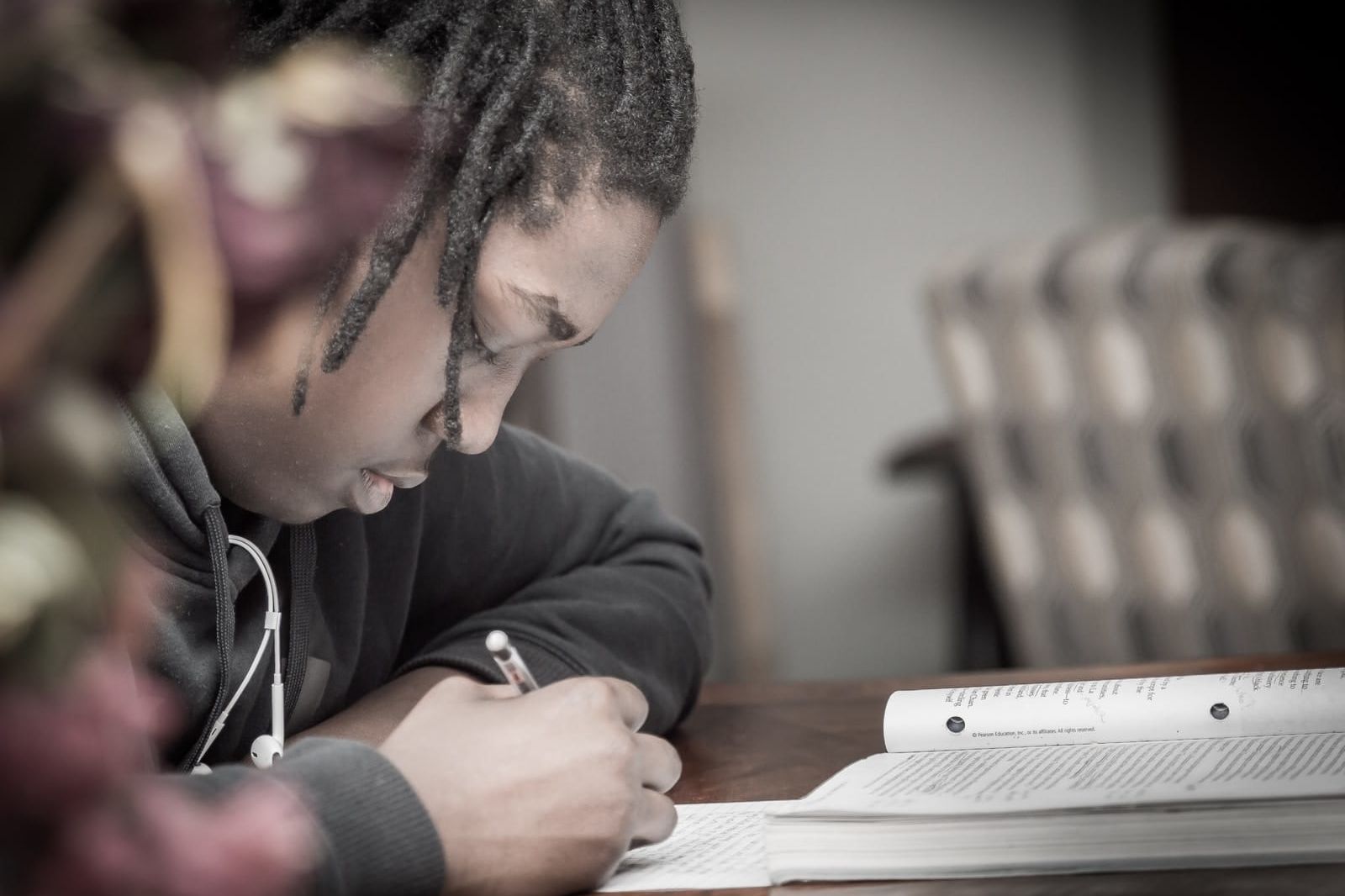 man writing on paper near book on table