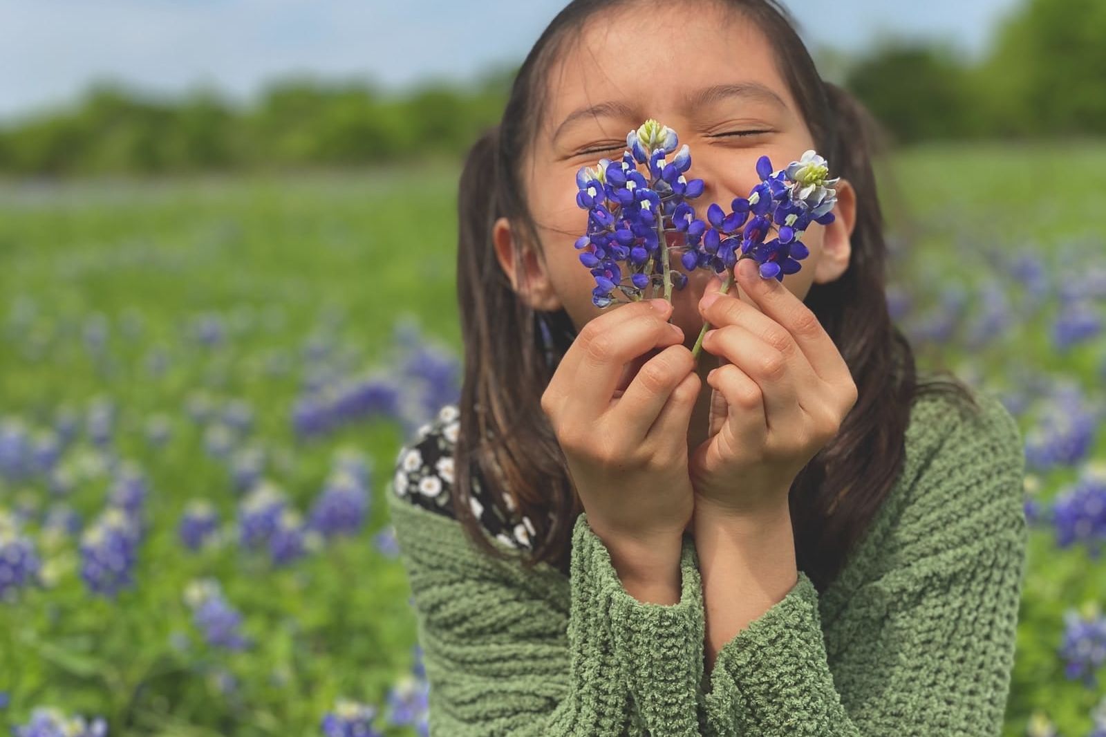 woman in green knit sweater holding blue flower