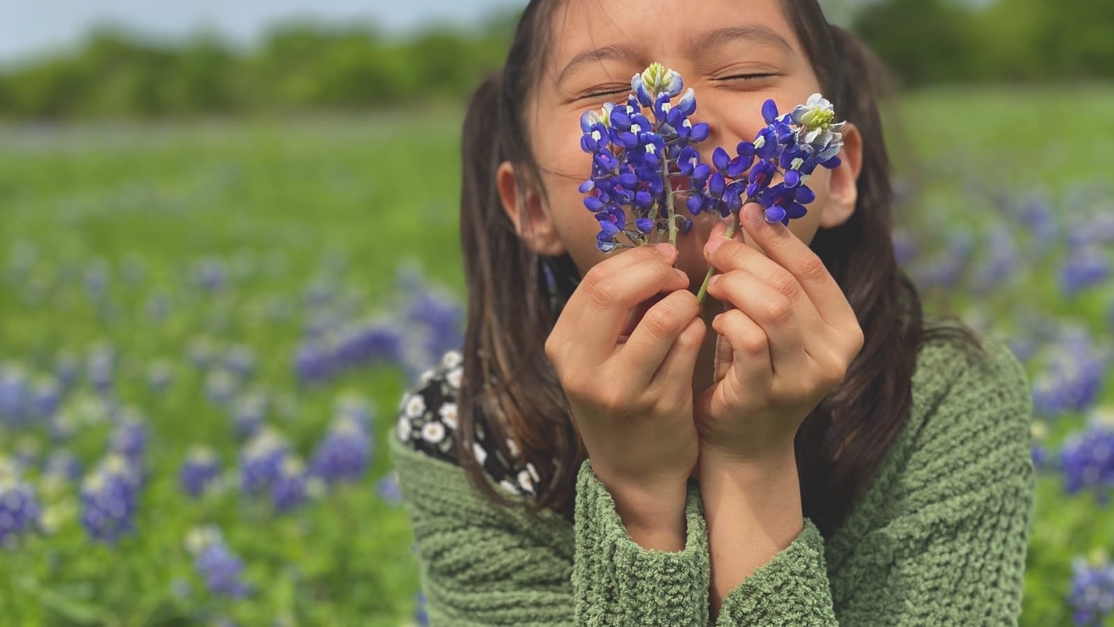 woman in green knit sweater holding blue flower