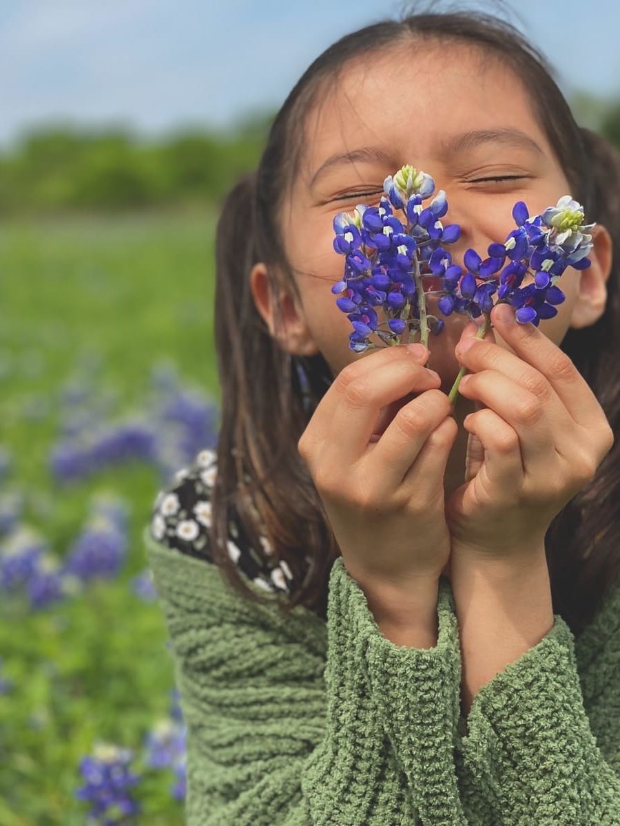 woman in green knit sweater holding blue flower