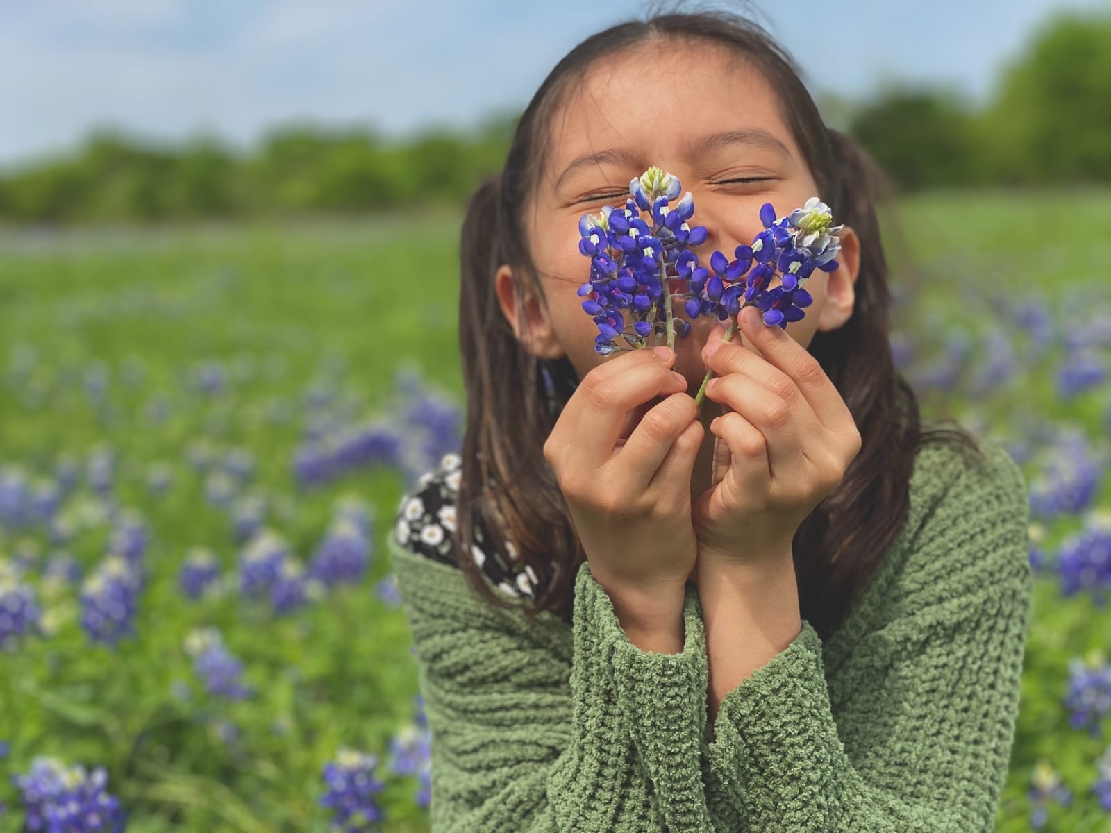 woman in green knit sweater holding blue flower