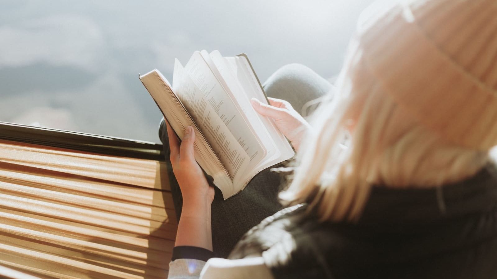 woman sitting on brown ledge while holding book