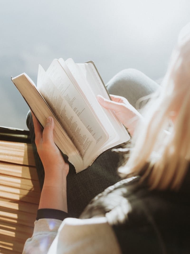 woman sitting on brown ledge while holding book