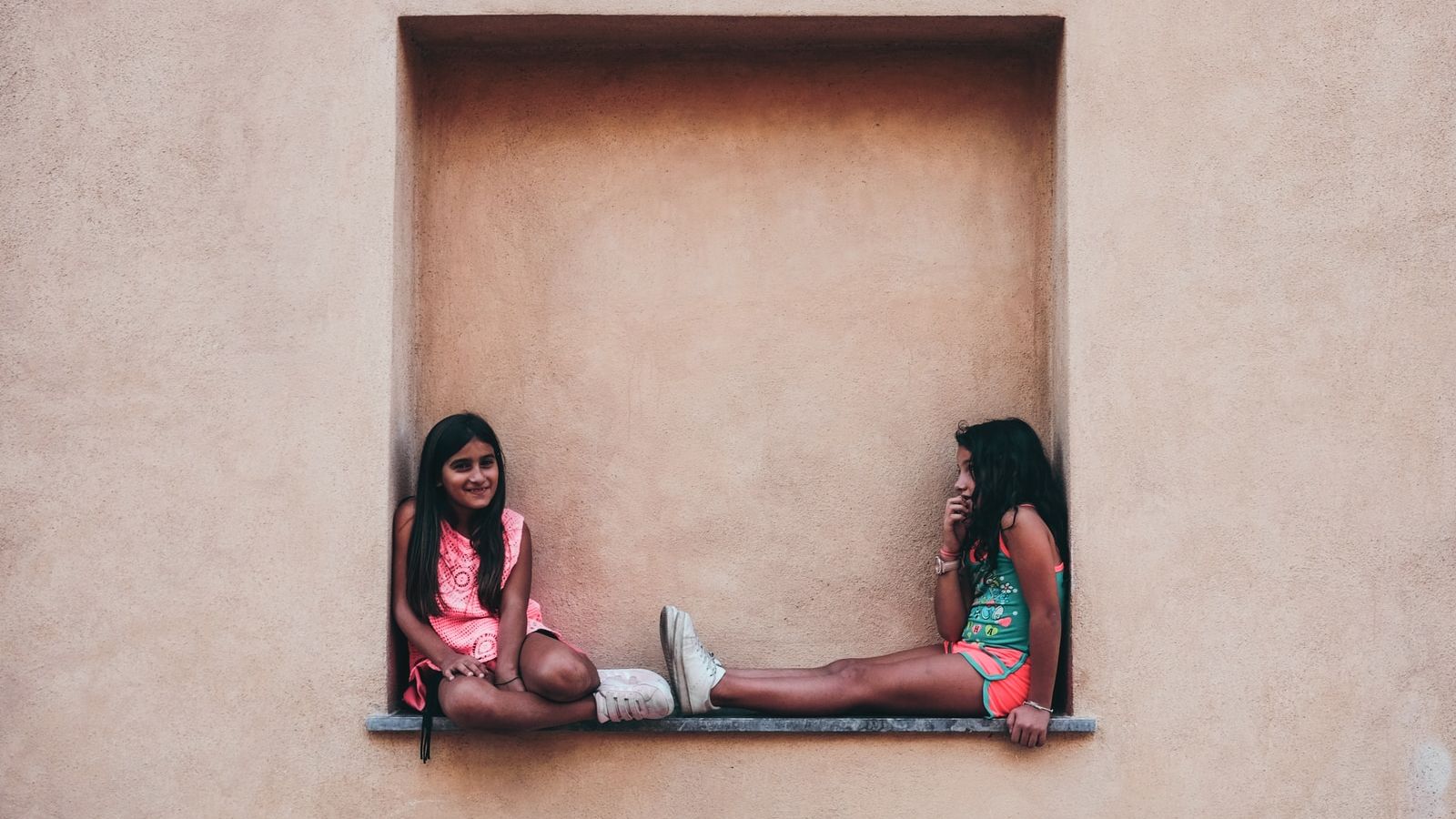 two girl in pink and green shirts sitting on wall shelf