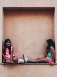 two girl in pink and green shirts sitting on wall shelf