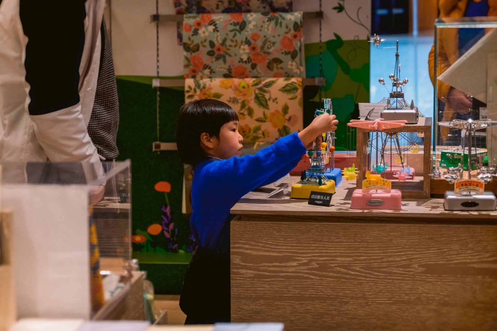 boy in blue long sleeve shirt standing beside brown wooden table