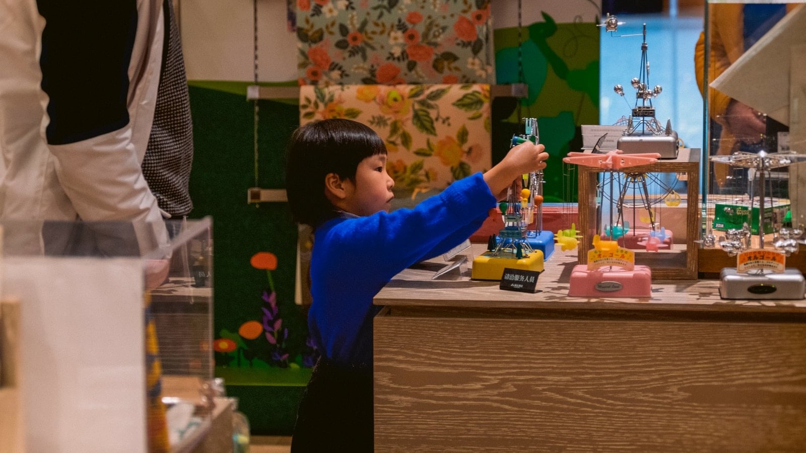 boy in blue long sleeve shirt standing beside brown wooden table