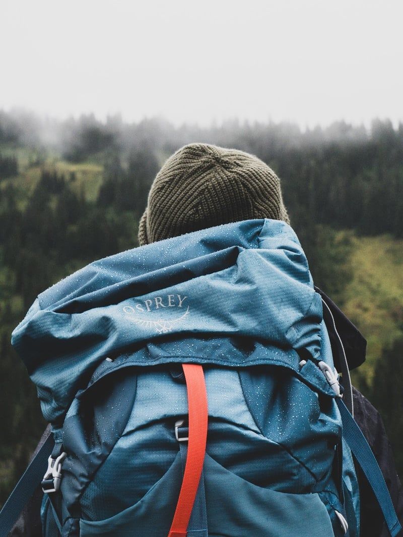 person wearing teal backpack looking at mountain