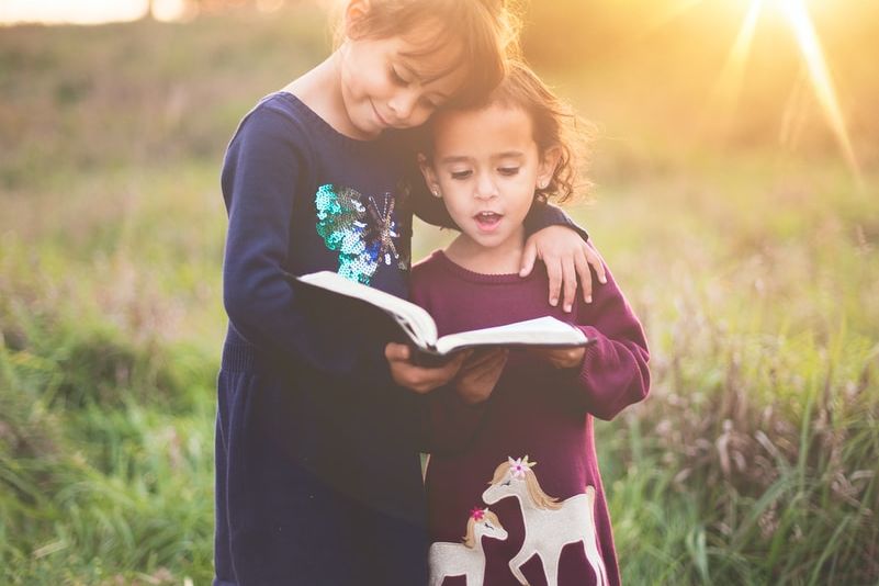 girl's left hand wrap around toddler while reading book during golden hour