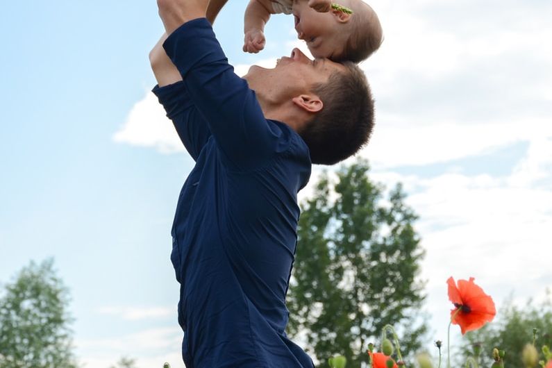 man in blue long sleeve shirt carrying baby in white onesie