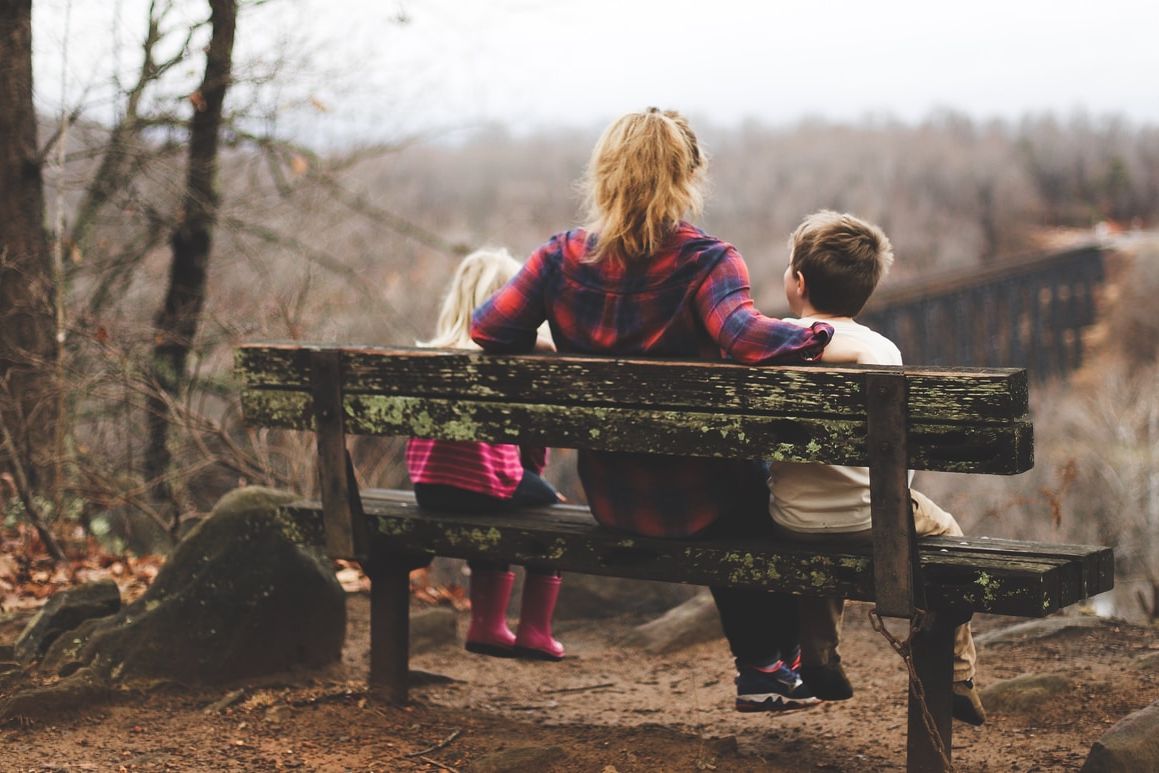 woman between two childrens sitting on brown wooden bench during daytime