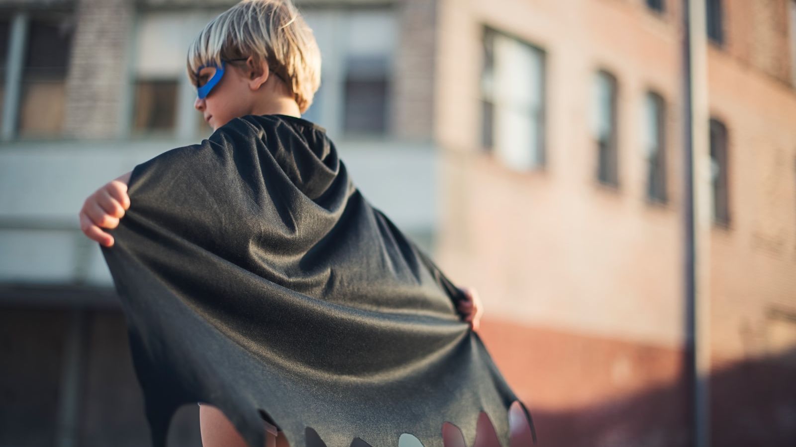 selective focus photography of boy wearing black Batman cape