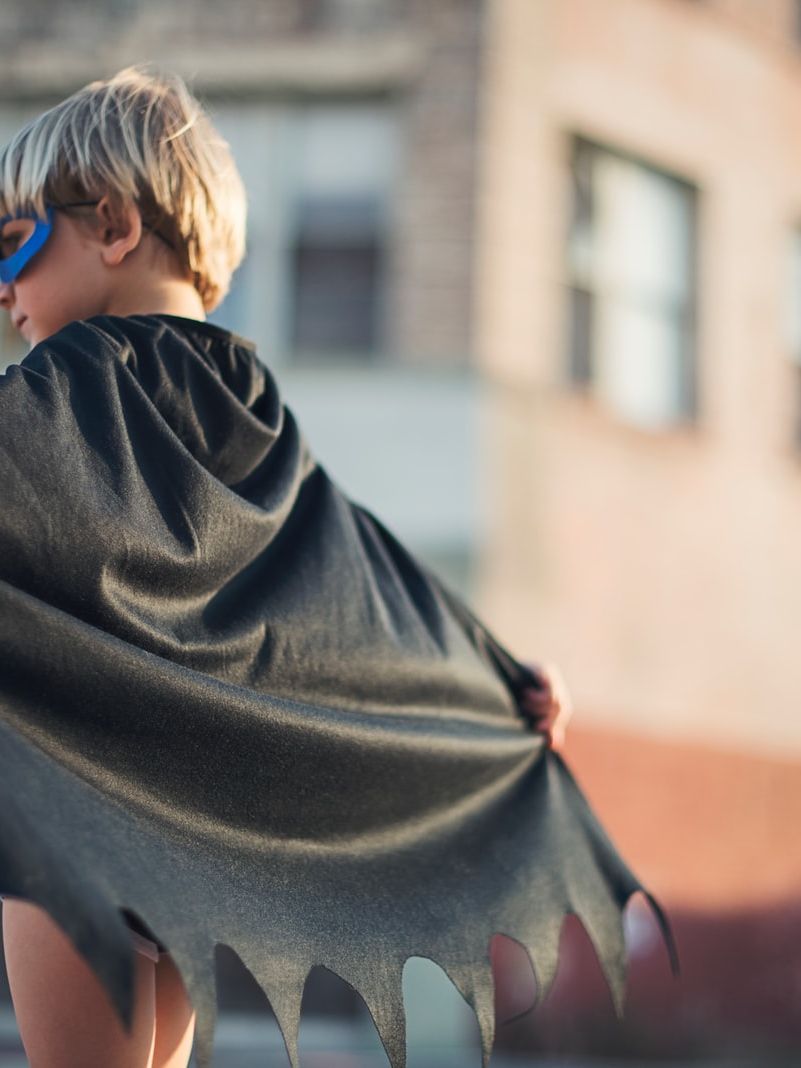 selective focus photography of boy wearing black Batman cape