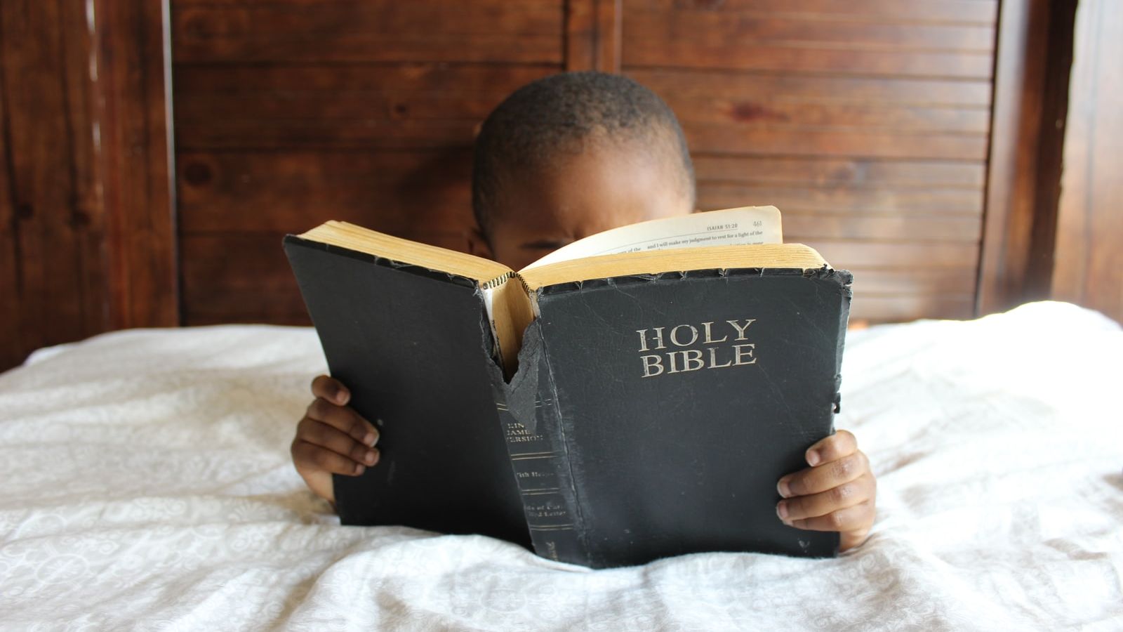 boy reading Holy Bible while lying on bed