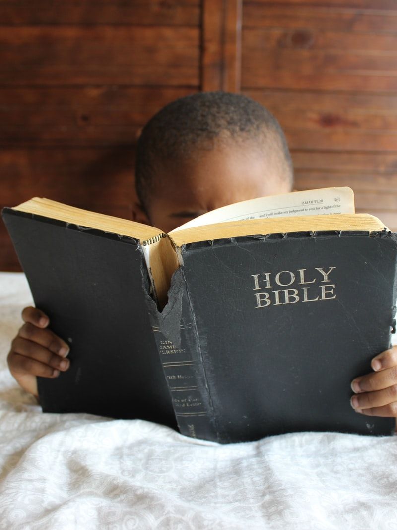 boy reading Holy Bible while lying on bed