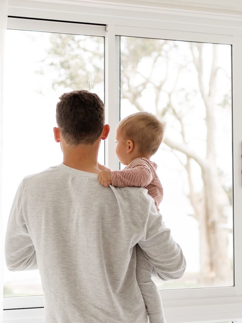 boy in gray sweater standing beside window during daytime