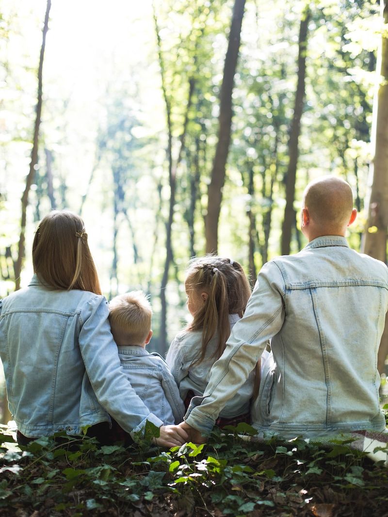 man and woman holding hands together with boy and girl looking at green trees during day