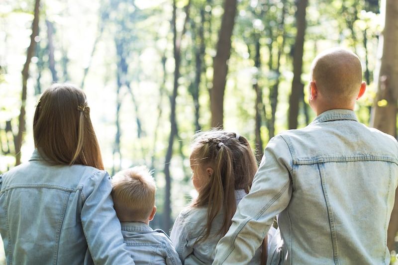 man and woman holding hands together with boy and girl looking at green trees during day