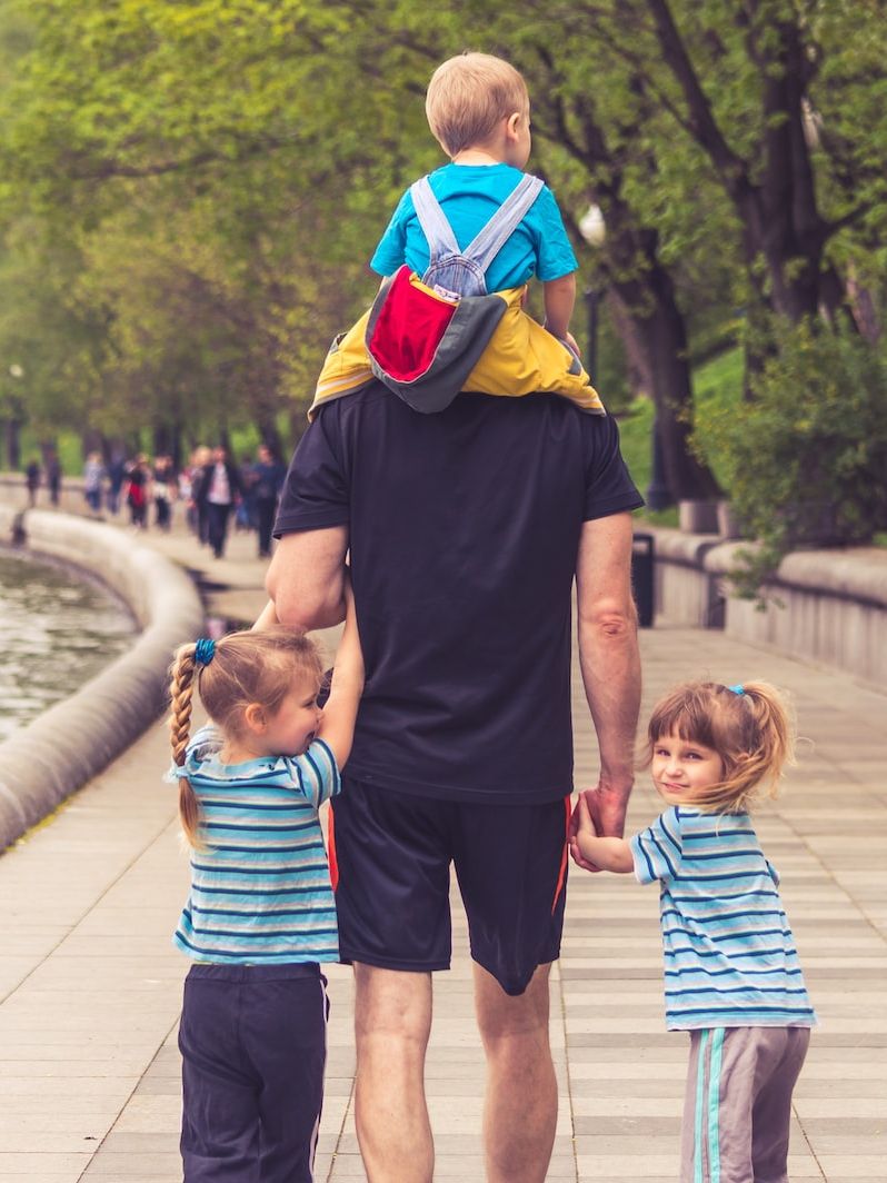 man in black t-shirt and brown shorts holding girl in blue and black jacket walking