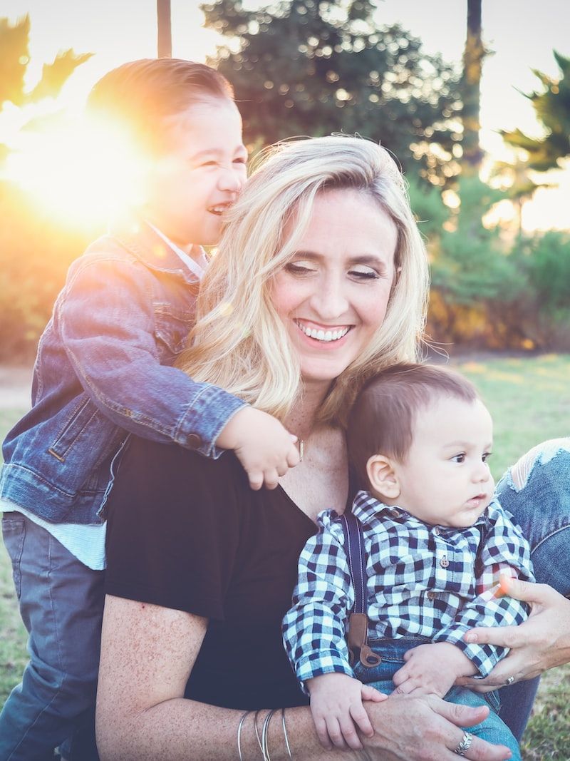 woman holding baby sitting on green grass field under sunset