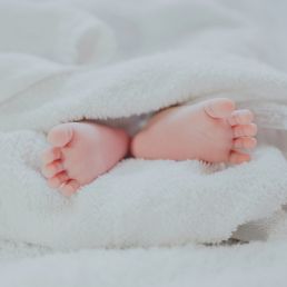 barefooted baby covering white blanket