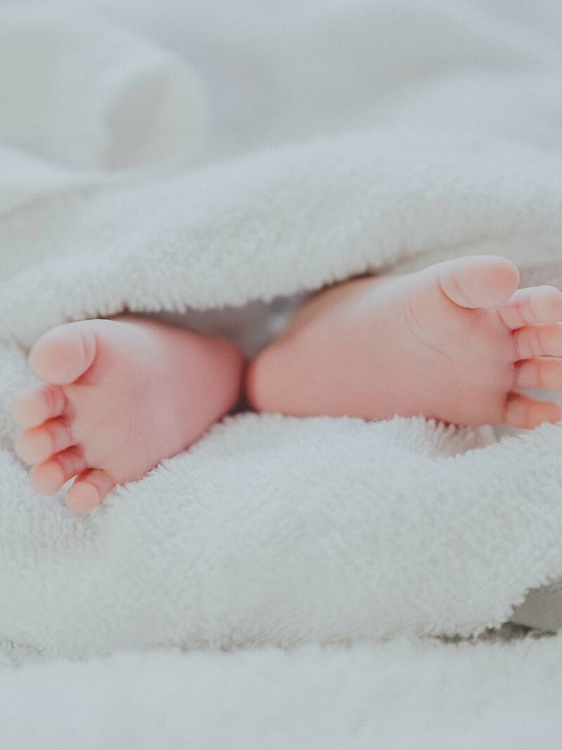 barefooted baby covering white blanket