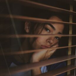 a woman looking out of a window with blinds