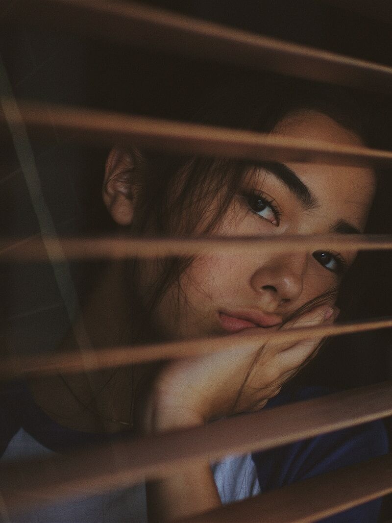 a woman looking out of a window with blinds